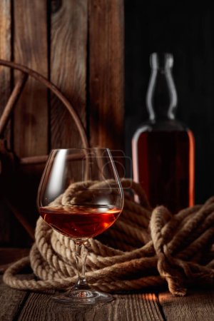 Foto de Snifter y botella con ron, coñac o whisky sobre un fondo de madera viejo. - Imagen libre de derechos