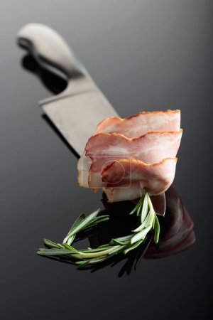 Photo for Bacon with rosemary on a kitchen knife. Reflective background. - Royalty Free Image