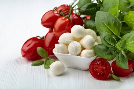 Photo for Mozzarella cheese with basil and tomatoes on a white wooden table. - Royalty Free Image