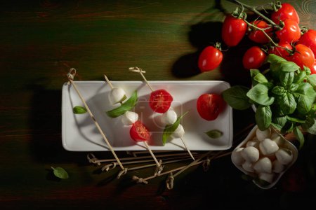 Foto de Queso mozzarella con albahaca y tomate sobre una mesa de madera verde oscuro. Vista superior. - Imagen libre de derechos