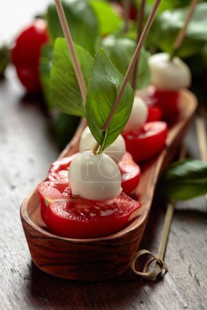 Téléchargez les photos : Mozzarella with basil and tomatoes on an old wooden table. Traditional Italian snack. - en image libre de droit