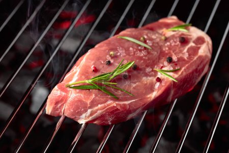 Téléchargez les photos : Raw steak on a grill with rosemary, pepper, and salt. - en image libre de droit
