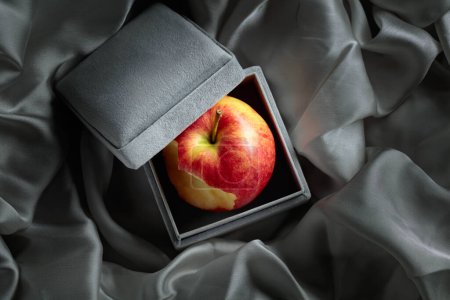 Téléchargez les photos : Une pomme mordue dans une boîte cadeau grise. Image conceptuelle sur le thème des cadeaux chers. - en image libre de droit