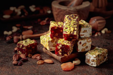 Photo for Turkish delight with nuts and dried fruits. Traditional east sweets on an old brown table with wooden kitchen utensils. - Royalty Free Image