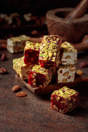 Foto de Turkish delight with nuts and dried fruits. Traditional east sweets on an old brown table with wooden kitchen utensils. - Imagen libre de derechos