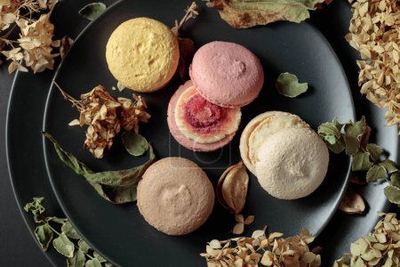 Photo for Delicious sweet colorful macaroons with dried flowers on a black plate. Top view. - Royalty Free Image