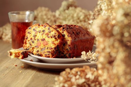 Photo for Cake with raisins and candied fruit. Fruit cake and tea on a wooden table with dried flowers. Selective focus. - Royalty Free Image