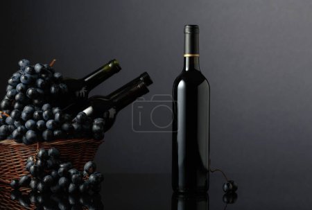 Téléchargez les photos : Red wine and blue grapes on a black reflective background. Focus on a bottle. - en image libre de droit