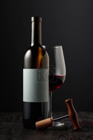 Photo for Red wine and corkscrew on black background. On a bottle empty label for your text. - Royalty Free Image