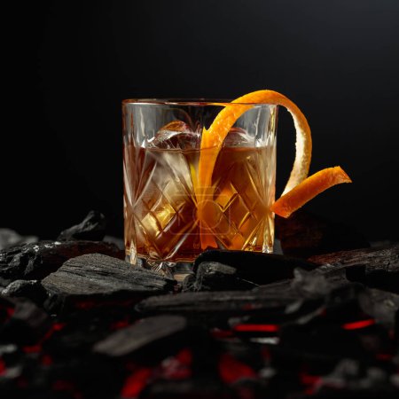 Photo for Whiskey with ice and orange peel. Glass with a cocktail on burning charcoal. - Royalty Free Image