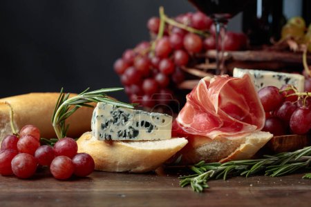 Photo for Sandwich with prosciutto, blue cheese and rosemary on a dark background. Delicious snack and grapes. - Royalty Free Image