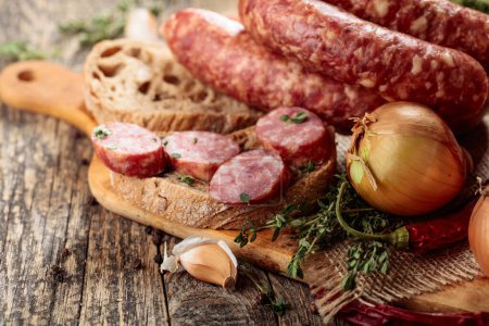 Photo for Dry-cured sausage with thyme, onion, garlic and pepper. Sausage with bread and spices on a old wooden table. - Royalty Free Image