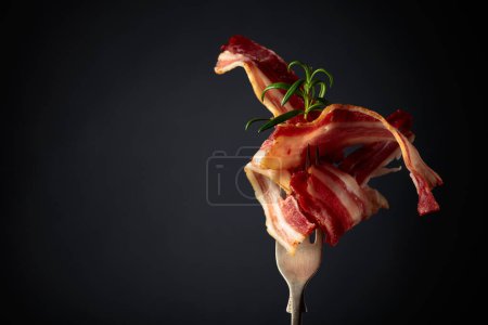 Téléchargez les photos : Tranches de bacon frit garnies de romarin sur fond noir
. - en image libre de droit