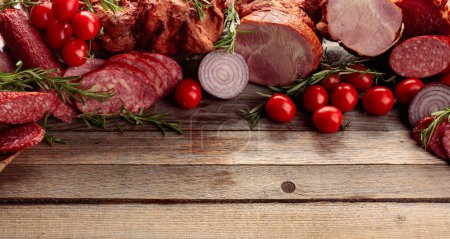 Photo for Salami, ham, fresh sausages, tomato, and rosemary on an old wooden table. Meat platter with a selection. Copy space. - Royalty Free Image