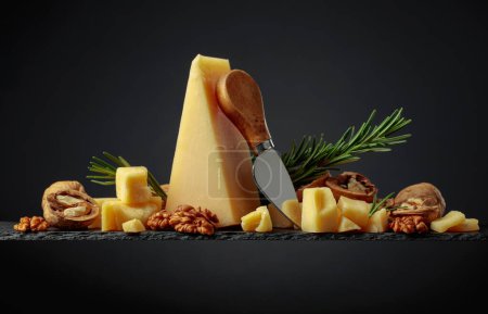 Foto de Parmesan cheese  with knife, rosemary, and walnuts on a black background. - Imagen libre de derechos