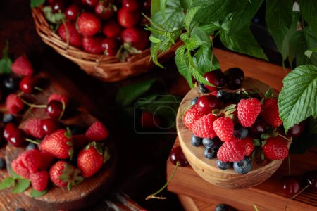 Foto de Surtido de bayas frescas con hojas. Fresas, frambuesas, arándanos y cerezas dulces en una mesa antigua. - Imagen libre de derechos