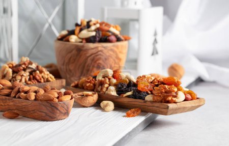 Téléchargez les photos : Mélange de noix et de raisins secs sur une table en bois blanc. Présenté raisins secs, noix, noisettes, noix de cajou, pacanes et amandes. - en image libre de droit