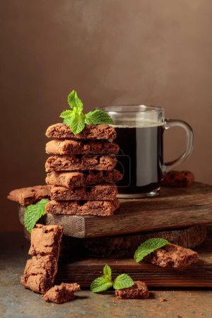 Téléchargez les photos : Pieces of fresh brownie with mint and a cup of black coffee on a rustic brown background. - en image libre de droit