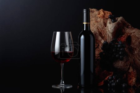 Photo for Bottle and glass of red wine. In the background old snag and grapes with dried-up vine leaves. Copy space. - Royalty Free Image