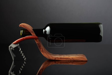 Foto de Botella de vino tinto en un portabotellas de madera y sacacorchos sobre fondo negro reflectante. Copiar espacio. - Imagen libre de derechos