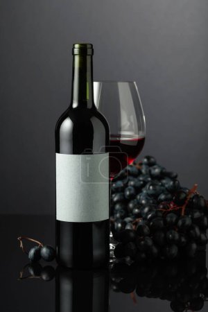 Photo for Red wine and blue grapes on a black reflective background. On the bottle old empty label. - Royalty Free Image