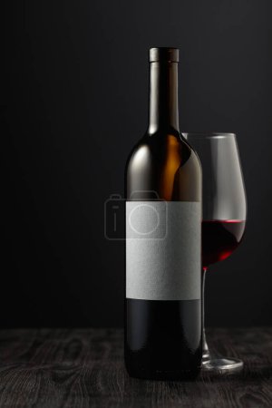 Téléchargez les photos : Bottle and glass of red wine on a black wooden table. On a bottle empty label with copy space for your text. - en image libre de droit