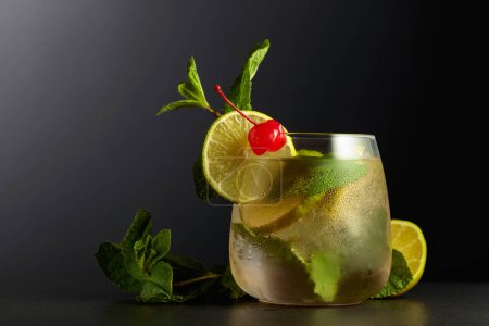 Foto de Cold refreshing drink with lime slices, mint, and cherry. Frozen glass with cocktail garnished with a preserved cherry. - Imagen libre de derechos