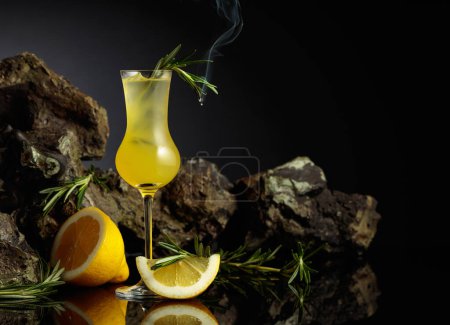 Foto de Italian traditional liqueur limoncello with lemon slices and smoldering rosemary branch. - Imagen libre de derechos