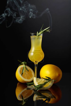 Foto de Italian traditional liqueur limoncello with lemon slices and smoldering rosemary branch. - Imagen libre de derechos