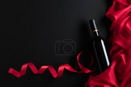 Téléchargez les photos : Bottle of red wine with red satin on a black background. Top view. - en image libre de droit