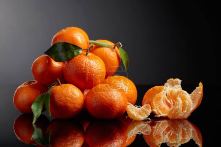 Téléchargez les photos : Tangerines or clementines with green leaves on a black reflective background. Copy space. - en image libre de droit
