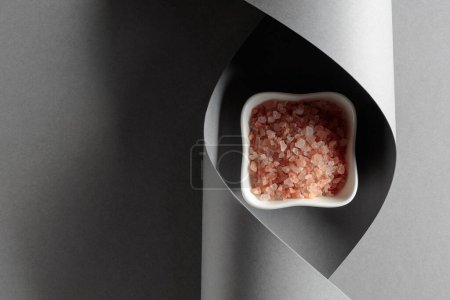 Foto de Sal rosa en un recipiente de cerámica blanca sobre un fondo gris. - Imagen libre de derechos