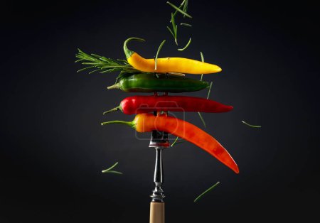 Foto de Colorful hot chili peppers sprinkled with rosemary on a black background. Concept of spicy food. - Imagen libre de derechos