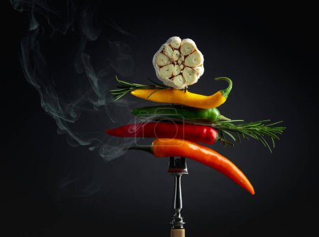 Foto de Red hot chili peppers with garlic and rosemary on black background. Concept of spicy food. - Imagen libre de derechos
