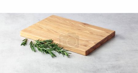 Téléchargez les photos : Cutting board and rosemary on a grey stone table. Isolated on a white background. Culinary background. Empty wooden cutting board, product display space. - en image libre de droit