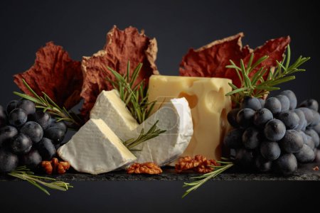Photo for Cheese with walnuts, blue grapes, and rosemary on a black background. Copy space. - Royalty Free Image