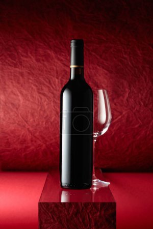 Téléchargez les photos : Bottle of red wine and an empty wine glass on a red background. - en image libre de droit