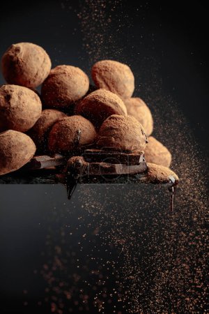 Téléchargez les photos : Délicieuses truffes au chocolat saupoudrées de cacao en poudre sur fond noir. - en image libre de droit