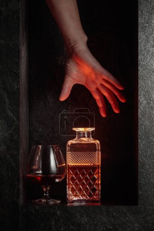 Téléchargez les photos : Hand reach for a decanter of brandy. A concept image on the theme of expensive drinks. - en image libre de droit