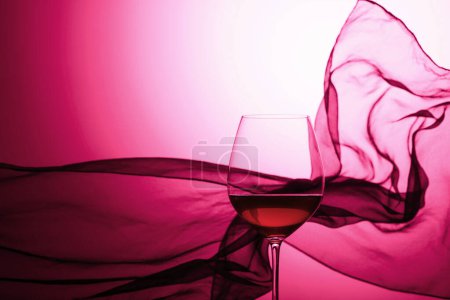 Foto de Copa de vino tinto sobre un fondo de cortina de satén ondulado. Púrpura retroiluminado. - Imagen libre de derechos