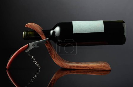 Téléchargez les photos : Bouteille de vin rouge avec une étiquette vide dans un porte-bouteille en bois sur un fond réfléchissant noir. Espace de copie. - en image libre de droit