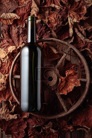 Téléchargez les photos : Bottle of red wine on the rusty wheel and dried-up vine leaves. Old expensive wine concept. Top view. - en image libre de droit