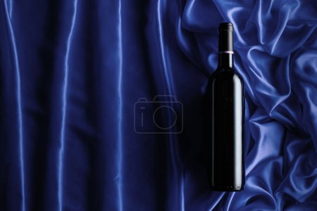 Foto de Bottle of red wine on a blue satin background. Top view. - Imagen libre de derechos
