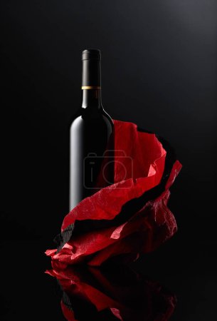 Téléchargez les photos : Une bouteille de vin rouge sur un papier froissé. Fond réfléchissant noir. - en image libre de droit