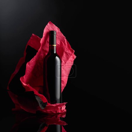 Téléchargez les photos : Bottle of red wine on a crumpled paper. Black reflective background. Copy space. - en image libre de droit
