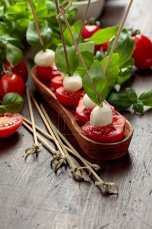 Photo for Mozzarella with basil and tomatoes on an old wooden table. Traditional Italian snack. Copy space. - Royalty Free Image