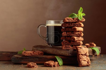 Foto de Pieces of fresh brownie with mint and a cup of black coffee on a rustic brown background. - Imagen libre de derechos