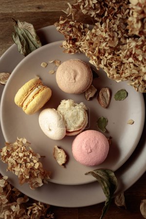 Photo for Delicious sweet colorful macaroons with dried flowers on a wooden table. Top view. - Royalty Free Image