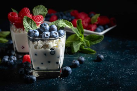Photo for Ricotta with cream, raspberries, and blueberries garnished with fresh mint on an old blue table. - Royalty Free Image