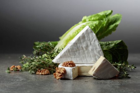 Foto de Queso Brie fresco con lechuga, tomillo y nueces sobre una mesa de piedra gris. - Imagen libre de derechos